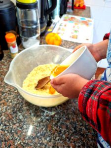 Child's hands pouring golden syrup into a butter and sugar mixture in a bowl, homemade cookie preparation process