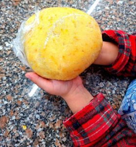 Child's hands holding a yellow ball of ginger and orange cookie dough wrapped in cling film, ready to rest in the fridge