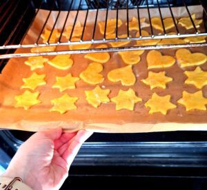 Two baking trays with star and heart shaped cookies going into the oven, arranged on baking paper, still unbaked