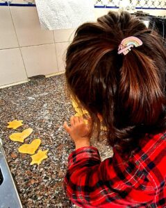 Child seen from behind cutting cookie dough with star and heart shaped cutters on the kitchen counter