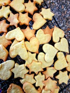 Bolachas caseiras de gengibre e laranja em forma de estrela e coração a arrefecer numa grelha preta, vista de cima
