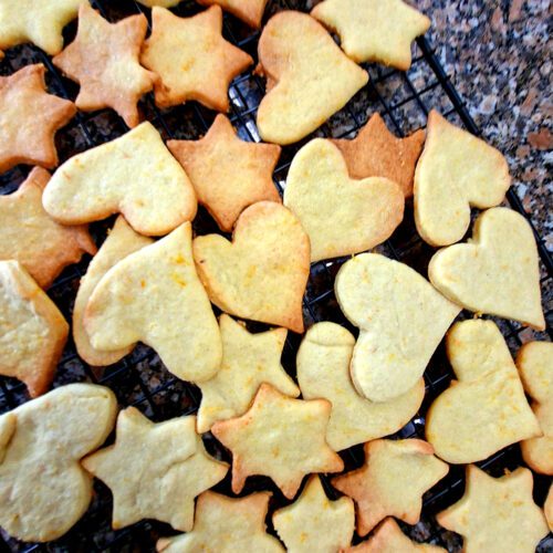 Bolachas caseiras de gengibre e laranja em forma de estrela e coração a arrefecer numa grelha preta, vista de cima