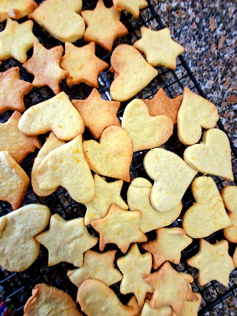Bolachas caseiras de gengibre e laranja em forma de estrela e coração a arrefecer numa grelha preta, vista de cima