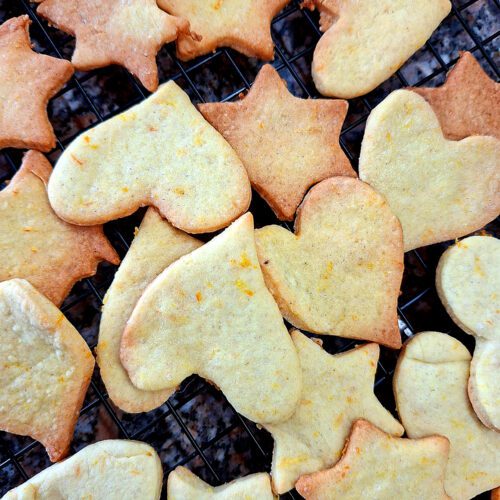Homemade ginger and orange cookies in star and heart shapes cooling on a black rack, top view