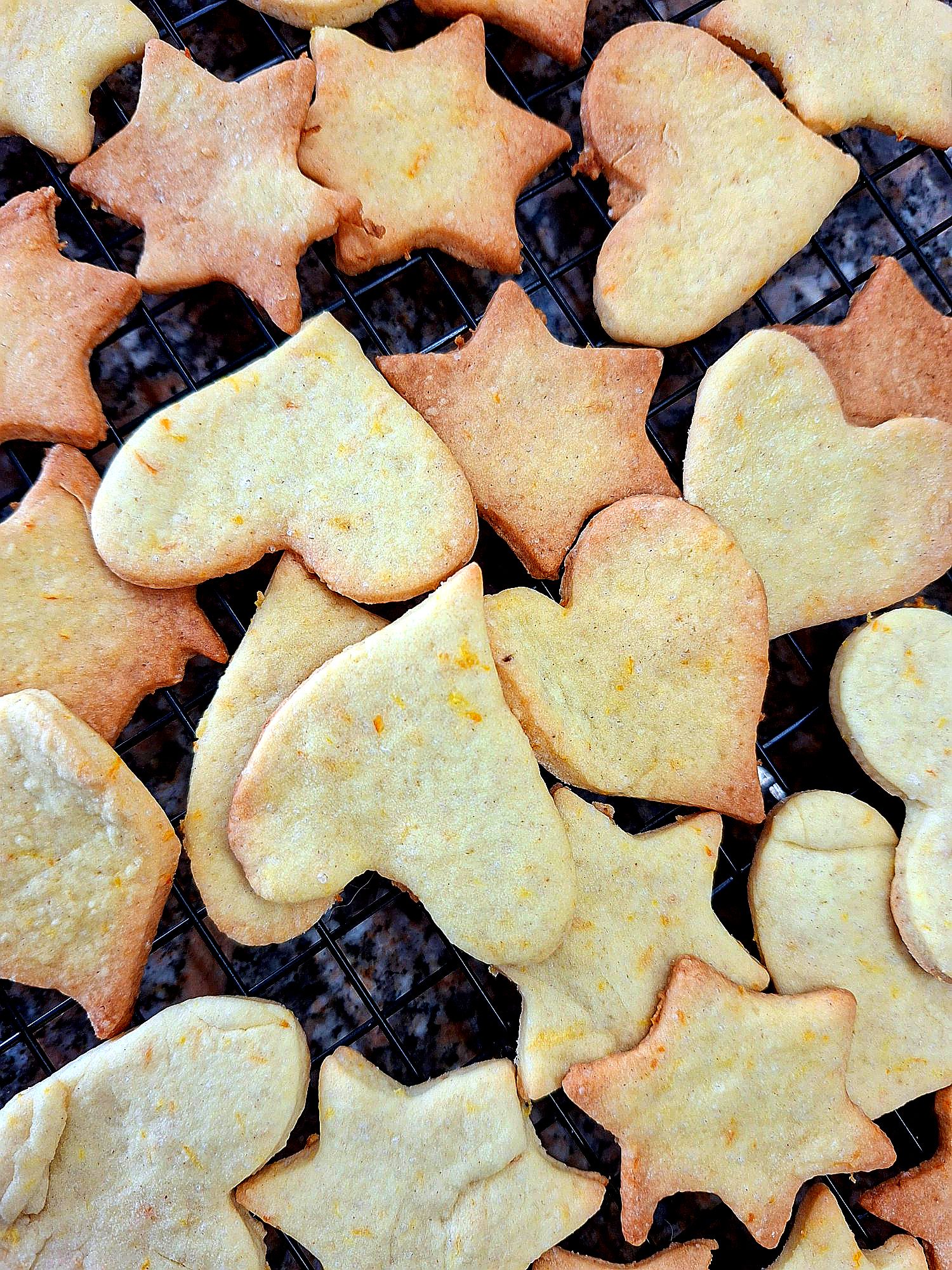 Homemade ginger and orange cookies in star and heart shapes cooling on a black rack, top view