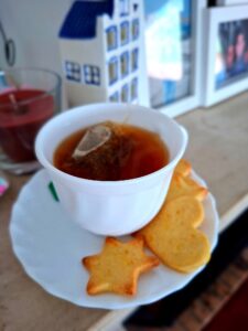 White teacup with teabag and homemade star and heart shaped cookies on the saucer, on a table with Portuguese azulejo house decoration in the background