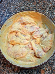 Taça com asinhas de frango cruas envolvidas numa marinada cremosa amarela, pousada sobre bancada de cozinha.