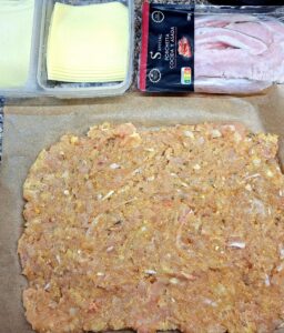 A filling of Flamengo cheese and porchetta spread over the raw chicken mixture, ready to roll