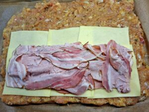 A filling of Flamengo cheese and porchetta spread over the raw chicken mixture, ready to roll