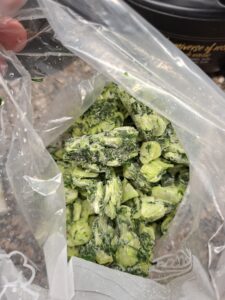 Saco de plástico transparente aberto com couve galega finamente picada e congelada, com cristais de gelo visíveis à superfície.