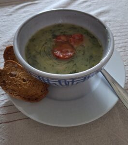 Blue and white faience bowl with geometric pattern containing caldo verde and chouriço slices, served with cornbread, seen from a slightly elevated frontal angle.