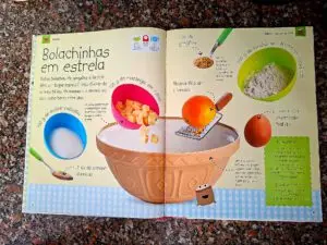 A two-page spread from the book featuring the “Star-Shaped Cookies” recipe, showing the ingredients photographed individually against a light background: sugar, cubed butter, golden syrup, ginger, orange zest, egg, and flour, with handwritten notes indicating the quantities.