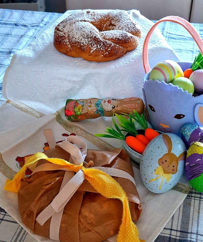 Table with powdered‑sugar Easter braid, bunny basket with colourful eggs and festive decorations.