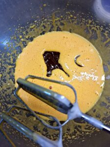Bowl with yellow cream and melted chocolate on top, with metal beaters ready to mix.