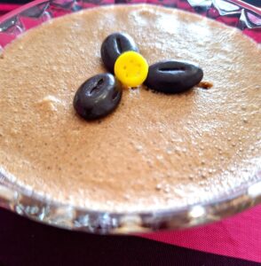 Glass bowl of chocolate mousse decorated with chocolate pieces and a small yellow candy.