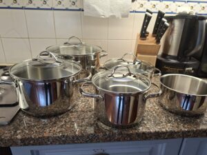 WMF Provence Plus polished stainless‑steel cookware set with glass lids arranged on a granite countertop, with a Tefal knife block and a kitchen robot in the background.