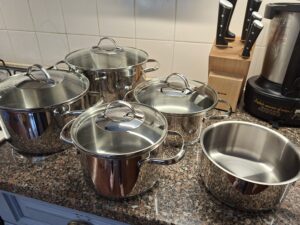 WMF Provence Plus stainless‑steel pots with glass lids on a granite countertop, side view, with a Tefal Ice Force knife block and a kitchen robot in the background.