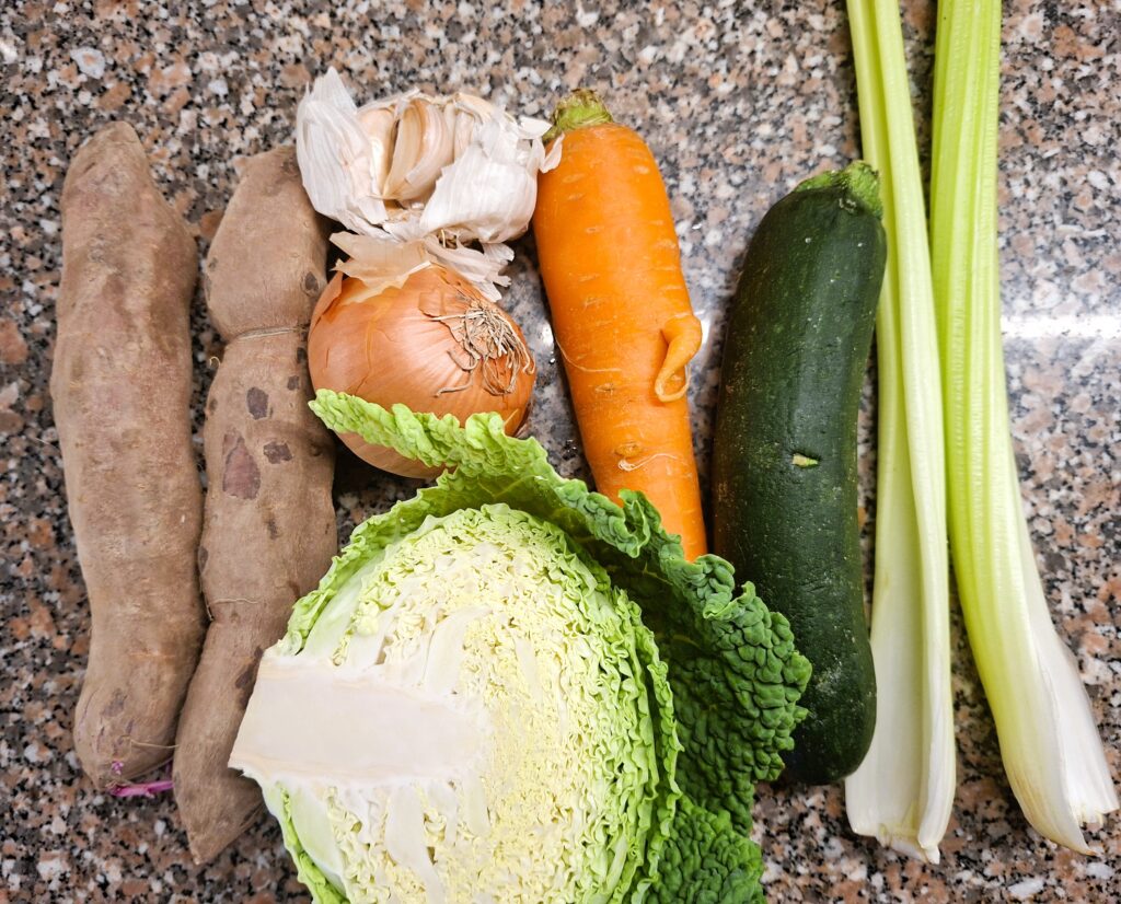 Assortment of fresh vegetables — sweet potatoes, garlic, onion, carrot, zucchini, celery and cabbage — arranged on a granite countertop.