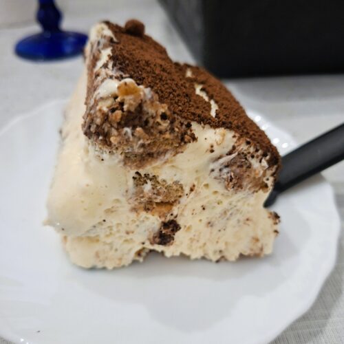 Close-up de uma fatia de tiramisu com camadas de creme e biscoitos, coberta com cacau em pó.