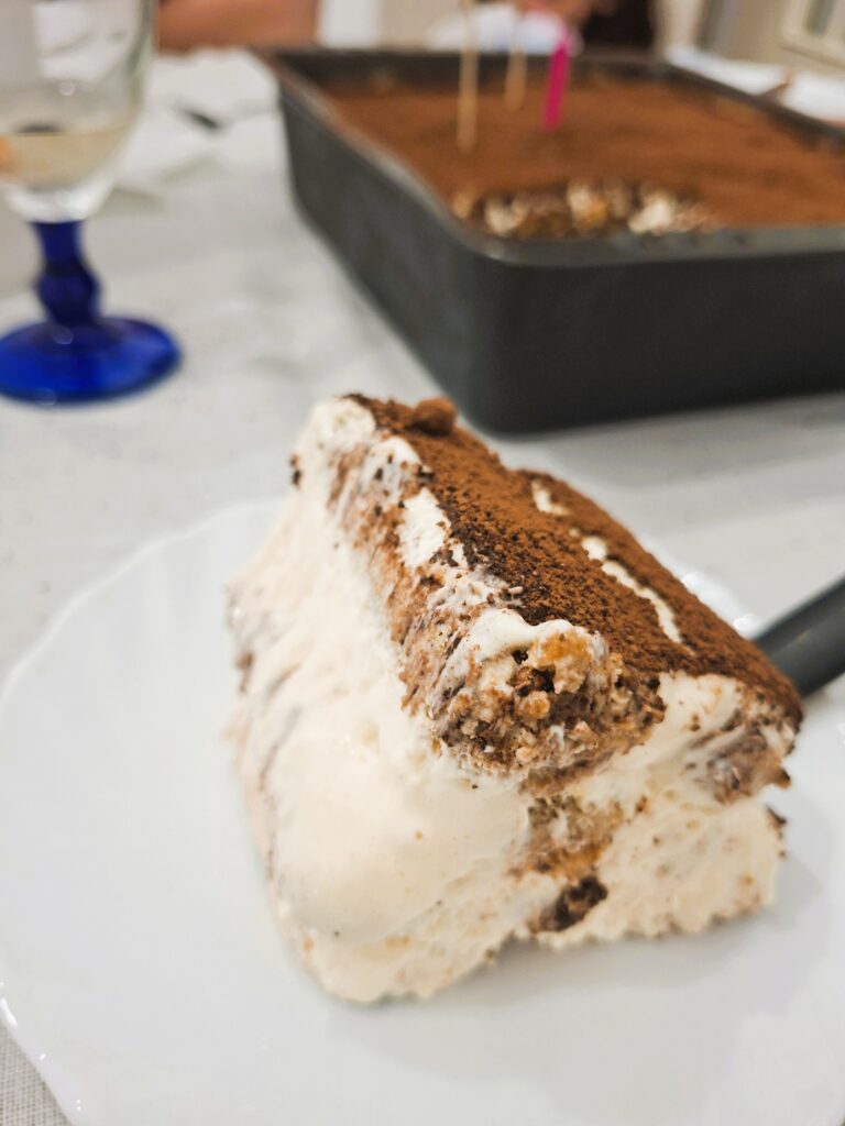 Close-up de uma fatia de tiramisu com camadas de creme e biscoitos, coberta com cacau em pó.