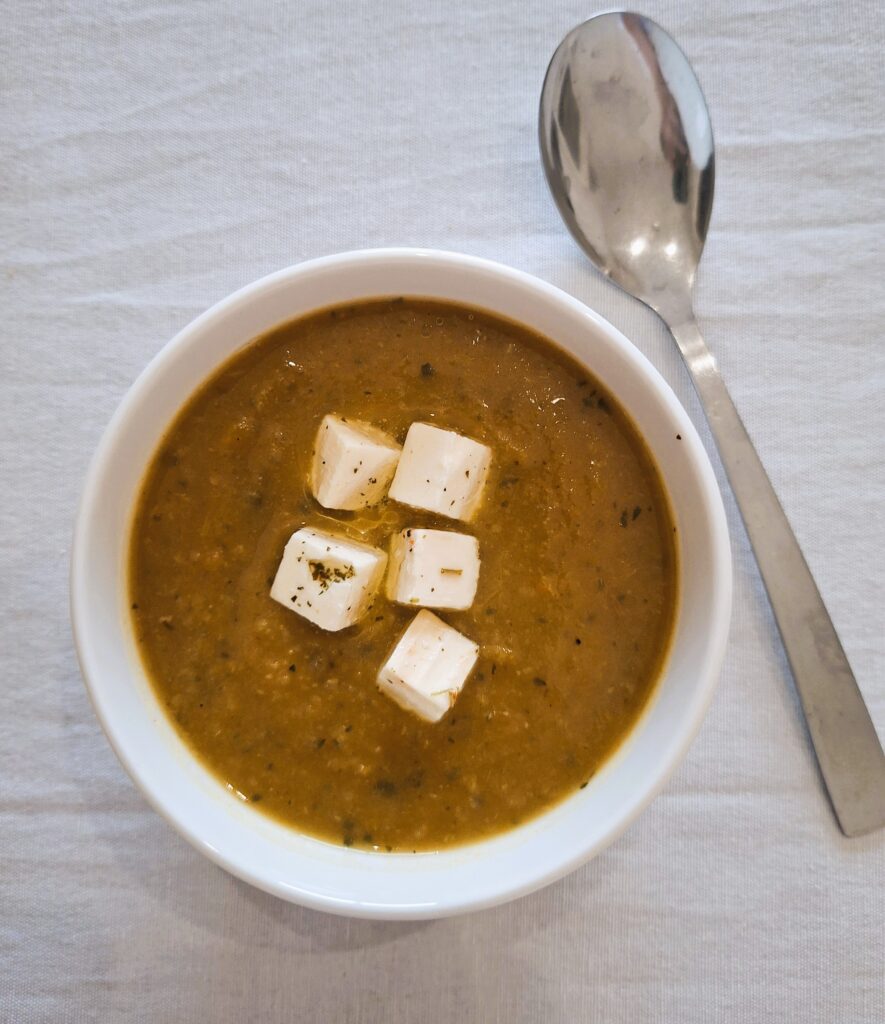 Bowl of thick brown soup topped with white cubes of cheese