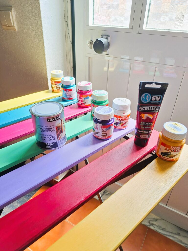 Several paint containers placed on wooden slats painted in vibrant colors.