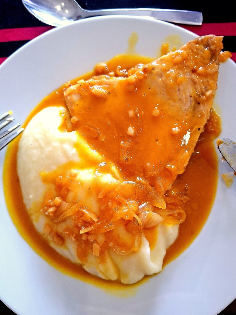 Close-up of swordfish served over mashed potatoes, topped with a thick sauce and bits of onion.