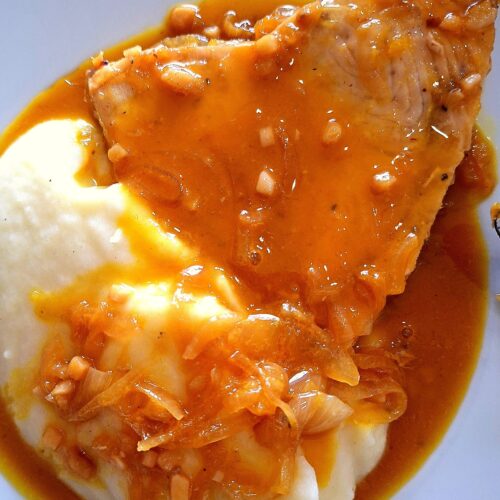 Close-up of swordfish served over mashed potatoes, topped with a thick sauce and bits of onion.