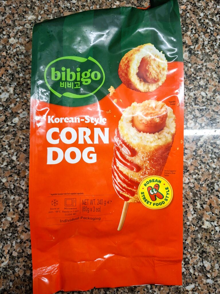 Package of Bibigo Korean-style corn dogs on a kitchen counter, with product image and green‑orange design.