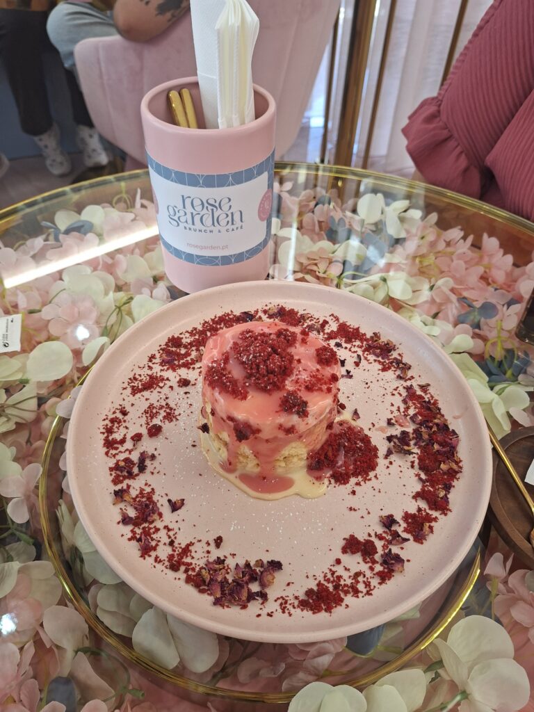 Sobremesa signature "pull me up" rosa decorada com pétalas e crumble, servida num prato pastel sobre mesa floral.
