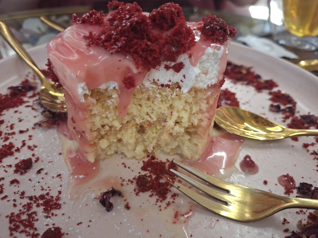Chá quente e sobremesa com Biscoff servidos sobre uma mesa de vidro decorada com pétalas cor‑de‑rosa, brancas e azuis.