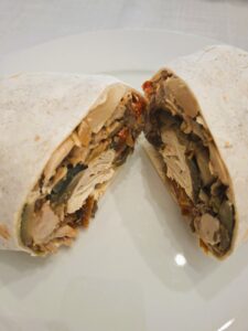 Close-up of a wrap cut in half, showing a filling of chicken, beans and roasted vegetables in the cross-section.