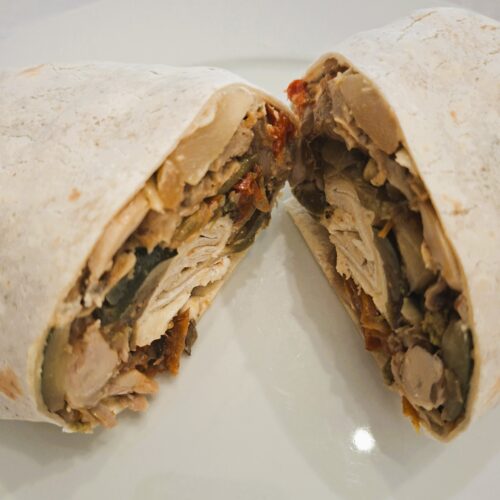 Close-up of a wrap cut in half, showing a filling of chicken, beans and roasted vegetables in the cross-section.