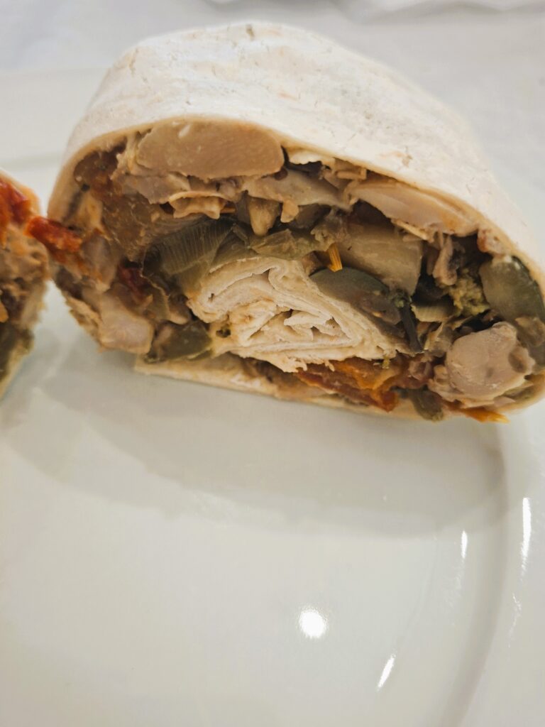 Wrap cut in half with a filling of roasted vegetables, mushrooms, courgette and sun-dried tomatoes, served on a white plate.