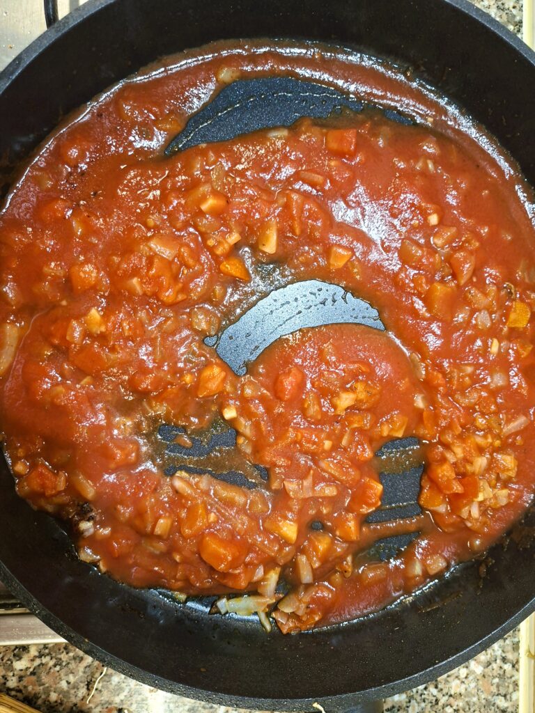 Molho de tomate caseiro a cozinhar numa frigideira, com pedaços de tomate e cebola.