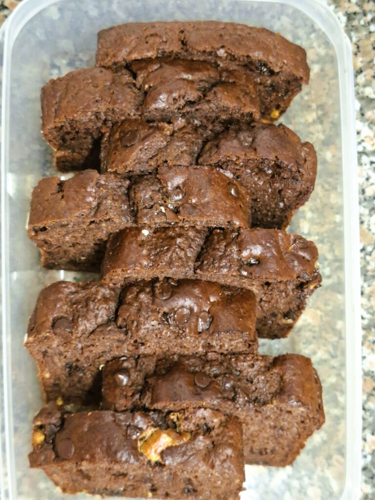 Slices of chocolate loaf arranged in a plastic container, showing a dense and moist crumb with chocolate chips.